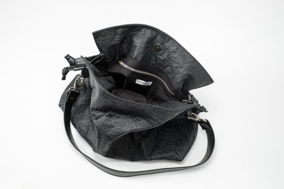 Top view on an open black Pinatex Bucket-Tote bag with a zip pocket and a white label sewn in the lining and a detachable shoulder strap made of vegan leather and a drawstring on each side of the bag