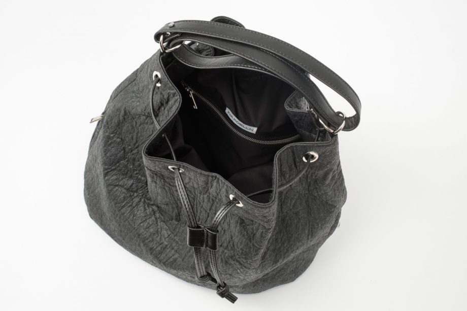 Top view on an open black Pinatex Bucket Bag with a zip pocket and a white label sewn in the lining and a three times folded adjustable handle made of vegan leather and a drawstring knotted in the front